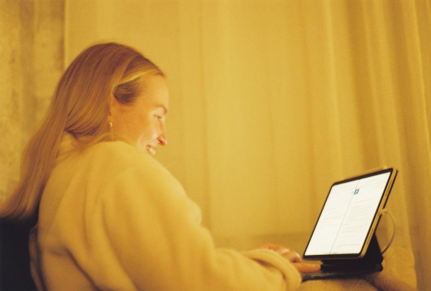 A person smiling at a tablet screen, lit by warm lamplight.